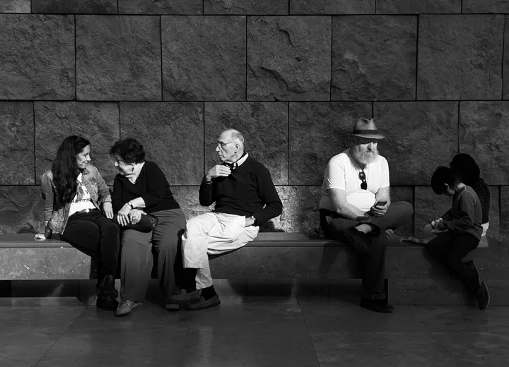 Grupa osób siedzących na ławce – różne pokolenia, każde ze swoją historią.